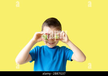 Lächelnder Junge hält eine Erdbeere in den Händen auf hellem Yelow-Hintergrund, Sommerferienkonzept Stockfoto