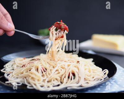 Hand in Hand mit leckerem Appetit klassische italienische Spaghetti-Pasta mit Tomatensauce, Käseparmesan und Basilikum darauf, Platte auf dunklem Tisch. Vie Stockfoto