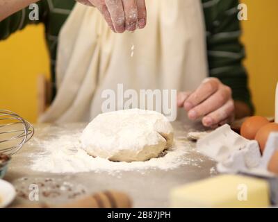 Männliche Hände, Koch, der Salz und Mehl zum Teig hinzufügt, der auf einem grauen Steintisch darauf arbeitet Stockfoto