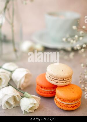 Makronen Kuchen und weiße Rosenblüten und eine Morgenschale Kaffee auf hellgrauem Steinteller. Wunderschönes Frühstück. Selektiver Fokus. Vertica Stockfoto