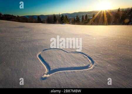 Herz trampelte auf dem Schnee mit Füßen in einer Schneeverwehung auf einem Hang mit herrlichem Blick auf den Nadelwald und die Bergketten auf einem sonnigen Frost Stockfoto