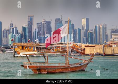 Katarische Flagge winkt auf einem traditionellen Holzboot, auch bekannt als Dhow an Corniche in Doha, Katar. Stockfoto