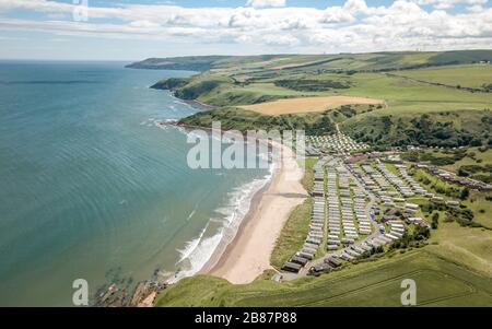 Statischer Wohnwagenpark und britische Landschaft. Luftdrone Blick auf die Küste, den sandigen Strand und die Ferienanlage mit Wohnwagen in Bucht und Tal. Stockfoto