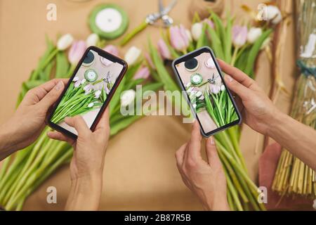 In der Nähe von zwei Frauen, die ein Smartphone-Foto von Tulpenblumen machen, während sie im Blumenladen arbeiten, kopieren sie Platz Stockfoto