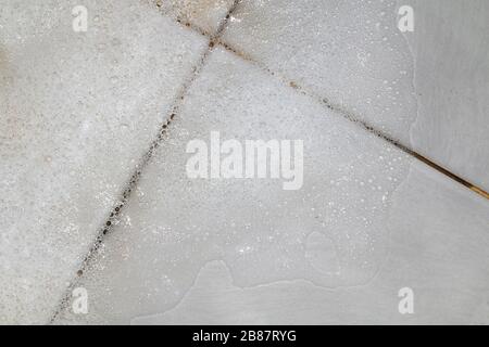 Seifenlauge mit Seifenlauge und Scheuern des Badezimmerbodens Schmutz nass, Schaumstoff weiße Seifenblase aus Shampoo waschen auf Fliesen Boden Draufsicht Stockfoto