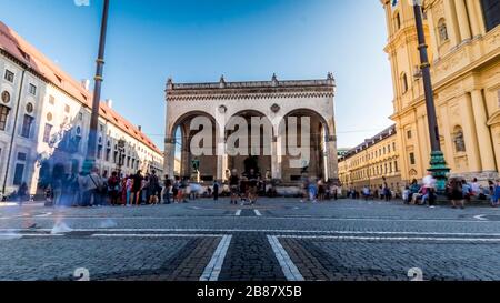 München 2019. Langzeitbelichtung von Touristen, die die Feldherrnhalle vom Odeonsplatz fotografieren. Wir sind am Nachmittag eines warmen und sonnigen Sommertags. Augu Stockfoto