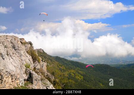 Extreme Erholung, Fallschirmspringer fliegt über die Berge und Felsen. Weiße Wolken am Himmel Stockfoto