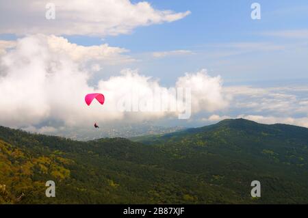 Extreme Erholung, Fallschirmspringer fliegt über die Berge und Felsen. Weiße Wolken am Himmel Stockfoto