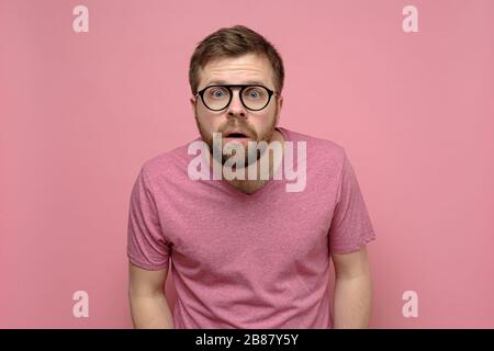 Mann mit Brille ist verwirrt, er lehnte sich nach vorne, blickt mit einem schockierten Gesichtsausdruck und glaubt nicht, was er gesehen hat. Stockfoto