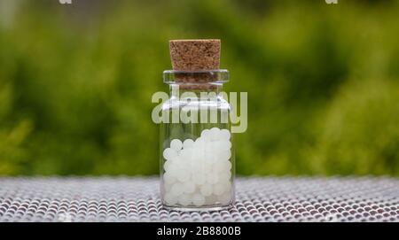 Homöopathie-Konzept. Homöopathische Globules in einer Glasflasche, grüner Hintergrund. Alternative Kräutermedizin Heilpflegemittel, Kopierraum Stockfoto