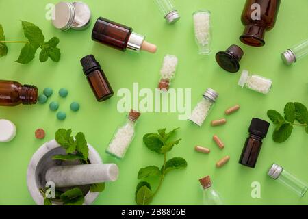 Homöopathie-Konzept. Glasflaschen und Fläschchen mit Homöopathika, flüssiger Substanz und frischen Kräutern, grünem Hintergrund. Alternative Kräutermedizin h Stockfoto