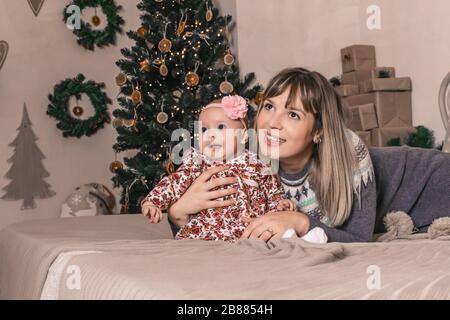 Fröhliche junge Mutter mit ihrem süßen Baby auf dem weihnachtsfoto Stockfoto