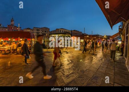 VENEDIG, ITALIEN - 02. August 2019: Die belebten Nachtsstraßen Venedigs. Die Leute gehen, entspannen, sitzen in zahlreichen Cafés. Nachtaufnahme mit langer Belichtung. Stockfoto