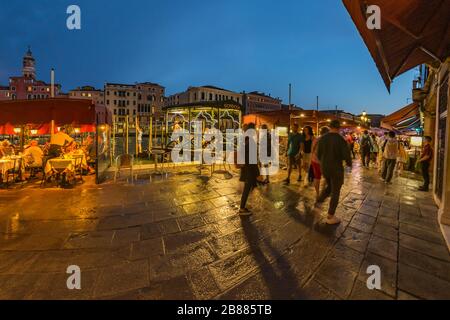 VENEDIG, ITALIEN - 02. August 2019: Die belebten Nachtsstraßen Venedigs. Die Leute gehen, entspannen, sitzen in zahlreichen Cafés. Nachtaufnahme mit langer Belichtung. Stockfoto