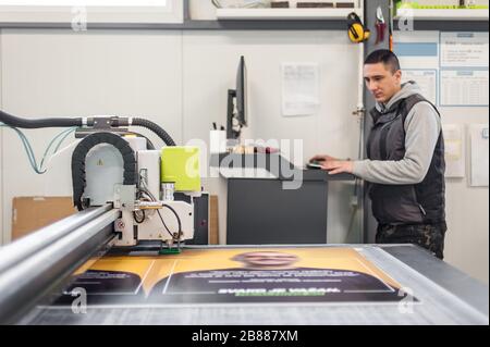 Der Techniker der Druckerei arbeitet an einer großen CNC-Computer- numerischen Steuerungs- und Schneidemaschine Stockfoto