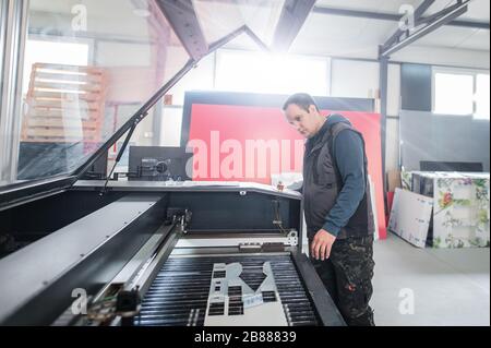 Der Techniker der Druckerei arbeitet an der Laser-CNC-Computer-numerischen Steuerungs- und Schneidemaschine Stockfoto