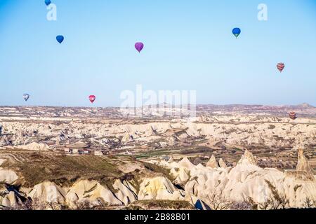 Panoramablick auf Heißluftballons am frühen Morgen im Flug, die über die aride, erodierte Feenkornsteinlandschaft von Gorome, Kappadokien, Türkei fliegen Stockfoto