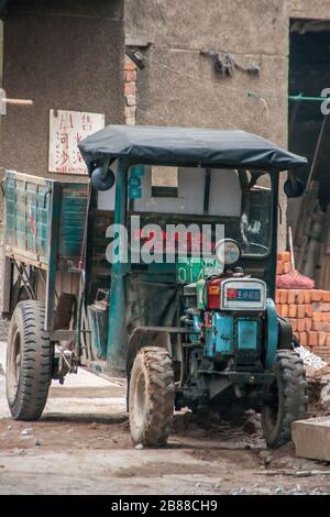 Guilin, China - 11. Mai 2010: Stadtzentrum. Grün-blauer Kleinschlepper mit freiliegenden Motoren an der Baustelle mit Stapel roter Ziegelsteine. Stockfoto