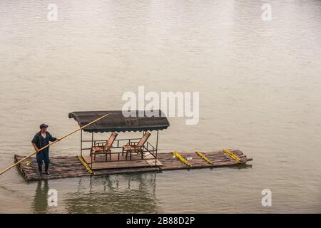 Guilin, China - 11. Mai 2010: Stadtzentrum. Nahaufnahme des Mannes, der Bambustaxi-Floß auf dem braunen Wasser Li River treibt. Stockfoto