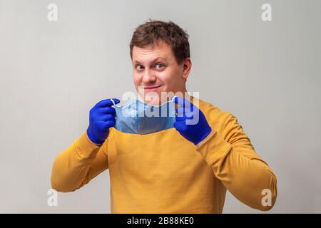 Ein junger Mann mit Handschuhen legt eine medizinische Maske an. Vorbeugung gegen Viruserkrankungen der häufigen Erkältung und Grippe. Hellgrauer Hintergrund. Europäischer Kerl in einer Atemmaske. Coronavirus und Kovid-19-Konzept Stockfoto