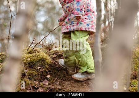 Tiefer Teil eines kaukasischen Kindermädchens in warmer Kleidung, das Anfang des Frühlings im März in Deutschland im Wald spielt Stockfoto