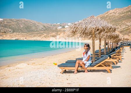 Frau Urlaub Mykonos Strand im Sommer mit Sonnenschirm und luxuriösen liegen, blaues Meer mit Berg am Elia Strand Mikonos Griechenland Stockfoto