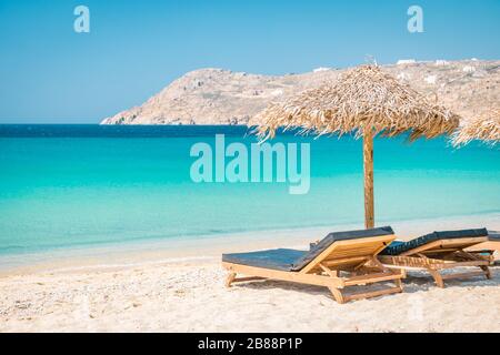 Mykonos Strand im Sommer mit Sonnenschirm und luxuriösen liegen, blaues Meer mit Berg am Elia Strand Mikonos Griechenland Stockfoto