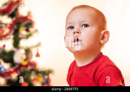 Ein kleiner Junge, der auf Geschenke vom Weihnachtsmann wartet, ist traurig und schreit in der Nähe des Neujahrsbaums. Stockfoto