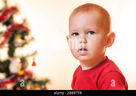 Ein kleiner Junge, der auf Geschenke vom Weihnachtsmann wartet, ist traurig und schreit in der Nähe des Neujahrsbaums. Stockfoto