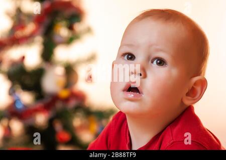 Ein kleiner Junge, der auf Geschenke vom Weihnachtsmann wartet, ist traurig und schreit in der Nähe des Neujahrsbaums. Stockfoto