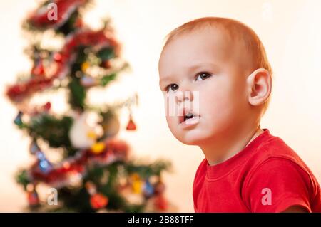 Ein kleiner Junge, der auf Geschenke vom Weihnachtsmann wartet, ist traurig und schreit in der Nähe des Neujahrsbaums. Stockfoto