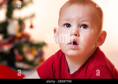 Ein kleiner Junge, der auf Geschenke vom Weihnachtsmann wartet, ist traurig und schreit in der Nähe des Neujahrsbaums. Stockfoto