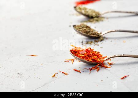 Safrangewürzt in einem alten Silberlöffel auf dem Hintergrund anderer Gewürze in Unschärfe auf grauem Betonhintergrund. Seitenansicht, Kopierbereich. Stockfoto