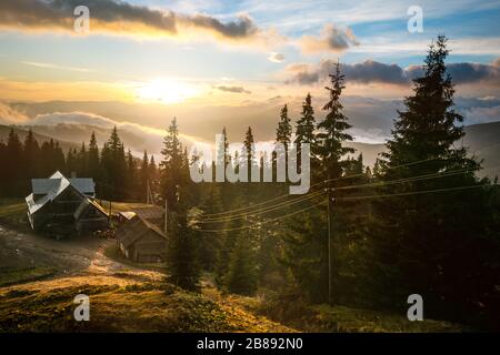 Kleines altes Holzhaus unter Baumbedeckten Hügeln. Berglandschaft, Nadelwald mit Nebel bedeckt Stockfoto