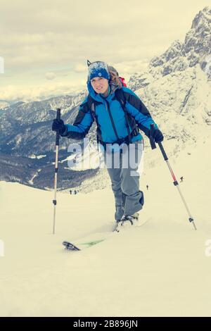 Weiblicher Skitourer mit aufsteigender schneebedeckter Bergabfahrt. Stockfoto