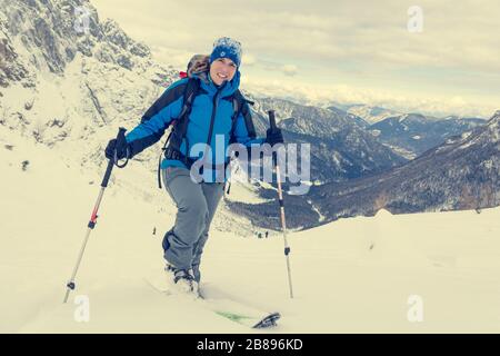 Weiblicher Skitourer mit aufsteigender schneebedeckter Bergabfahrt. Stockfoto