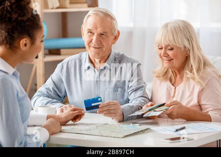 Reisebüro im Büro mit älteren Kunden Mann mit Kreditkarte und Frau mit Pässen und Tickets glücklich sitzen Stockfoto