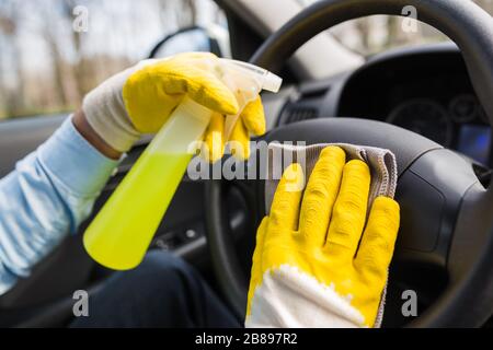 Das Autolenkrad mit Mikrofasertuch reinigen und die Sprühflasche mit Desinfektionsmittel halten. Stockfoto