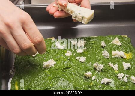 Hausfrau händigt dem rohen Spinat Lasagna den schimmeligen Käse aus Stockfoto