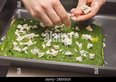 Hausfrau händigt dem rohen Spinat Lasagna den schimmeligen Käse aus Stockfoto