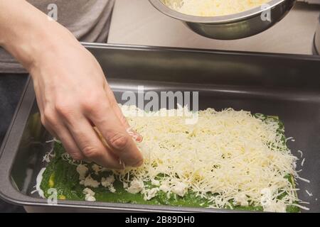 Hausfrau legt geriebenen Käse auf rohen Spinat Lasagna Stockfoto