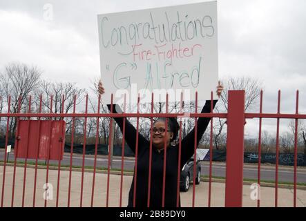 St. Louis, USA. März 2020. Rivian Robinson hält ein Schild für ihren Sohn, den St. Louis Feuerwehrmann Gavin Alfred, um zu sehen, während er nach Abschlussfeiern in St. Louis am Freitag, den 20. März 2020, über einen Parkplatz spaziert. Robinson und alle Familienmitglieder der 40 Absolventen konnten wegen der vom Staat Missouri und der Stadt St. Louis eingeführten Richtlinien zur sozialen Distanzierung nicht an den Abschlussfeiern der Feuerwehr von St. Louis teilnehmen. Personen dürfen nicht gleichzeitig in Gruppen größer als 10 sein. Foto von Bill Greenblatt/UPI Credit: UPI/Alamy Live News Stockfoto