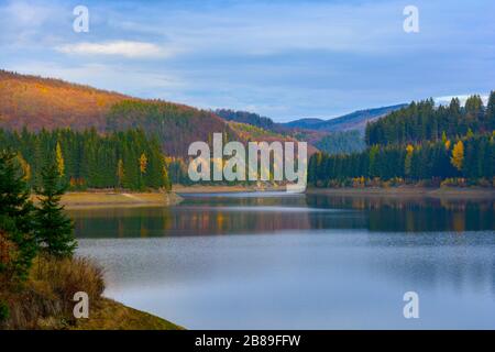 Wunderbarer See mit sauberem Wasser, der die runden Berge widerspiegelt, die von immergrünen Tannenwäldern und Fichten bedeckt sind Stockfoto