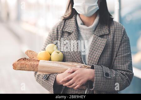 Junge Frau, die Essen auf der Straße spazieren hält und im Freien eine medizinische Maske trägt. Soziale Distanzierung. Virus-Konzept. Stockfoto