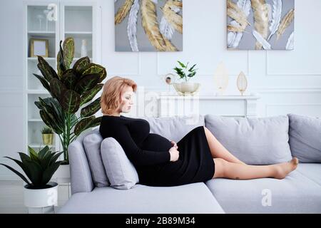 Schwangere Frau in schwarzem Kleid lächelnd berühren Bauch Stockfoto