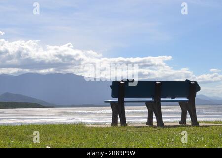 Leere Parkbank mit Blick auf den Mündungseingang in Port Douglas, Queensland in Australien an einem sonnigen warmen Tag Stockfoto