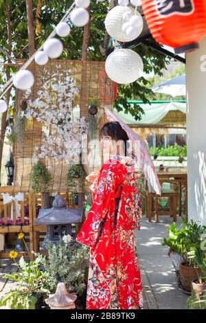 Das Mädchen trägt einen roten traditionellen Kimono, das ist das Nationalkleid Japans und hat einen Regenschirm Stockfoto