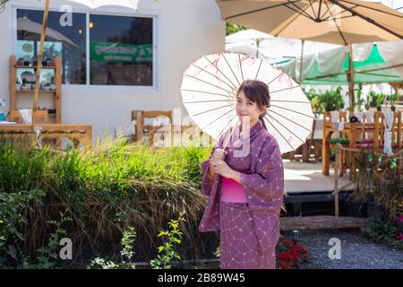 Das Mädchen trägt eine rosafarbene traditionelle Yukata, die das Nationalkleid Japans ist und einen Regenschirm hält Stockfoto