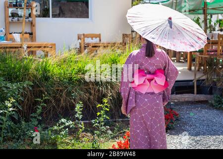 Das Mädchen trägt eine rosafarbene traditionelle Yukata, die das Nationalkleid Japans ist und einen Regenschirm hält Stockfoto
