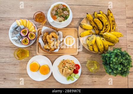 Frühstück mit Milch, Orangensaft, Croissants, gebratenem Reis mit Obst und Brot auf Holztisch. Ausgewogene Ernährung. Stockfoto